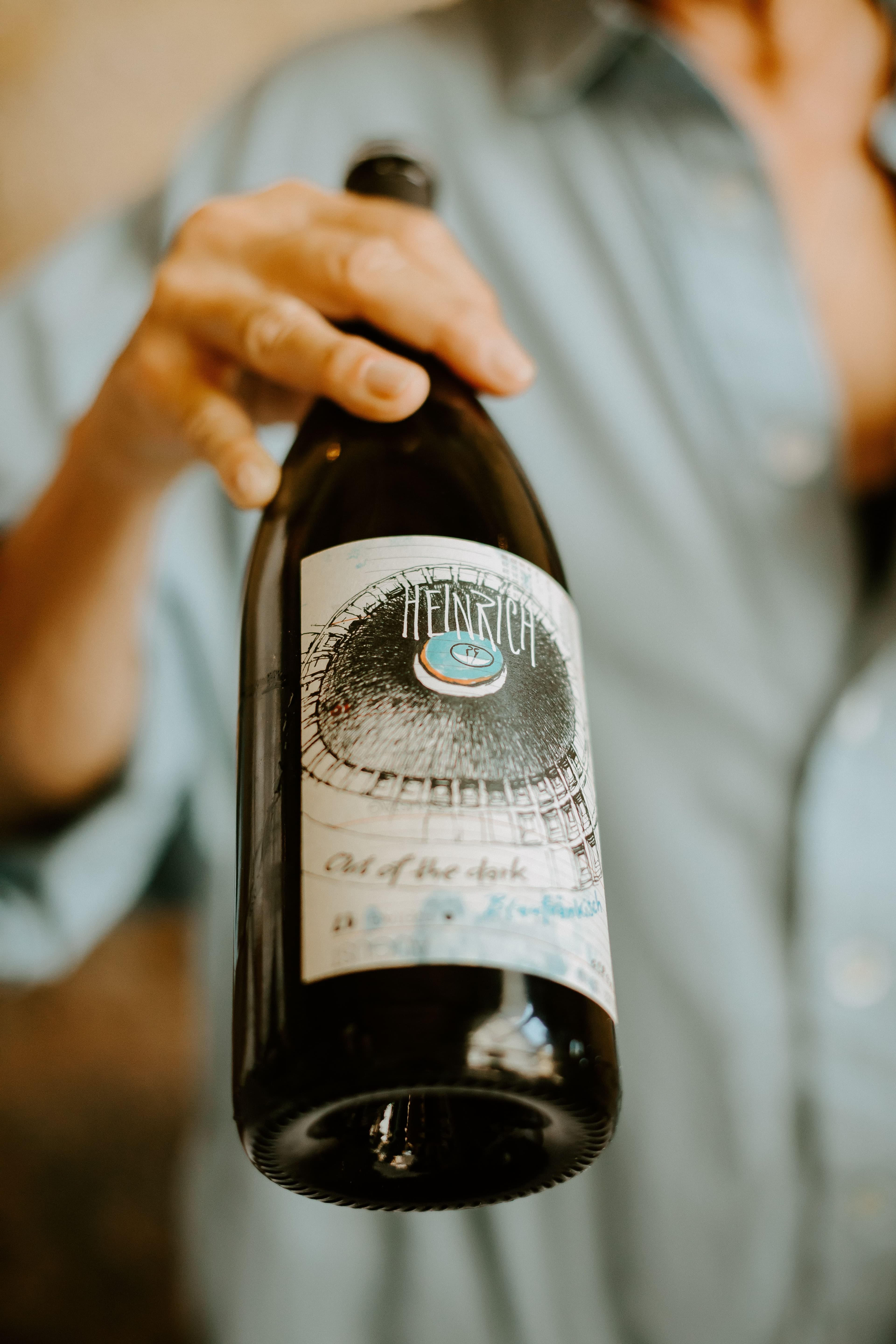 A wine bottle is presented by a person in a blue shirt.