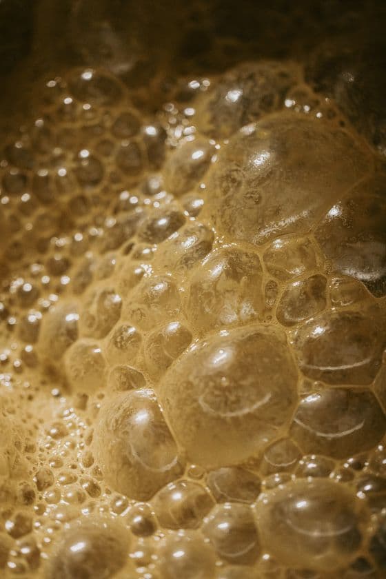 Close-up of beige soap bubbles with various sizes and reflective surfaces, creating a textured and dynamic pattern. The mood is playful and delicate.